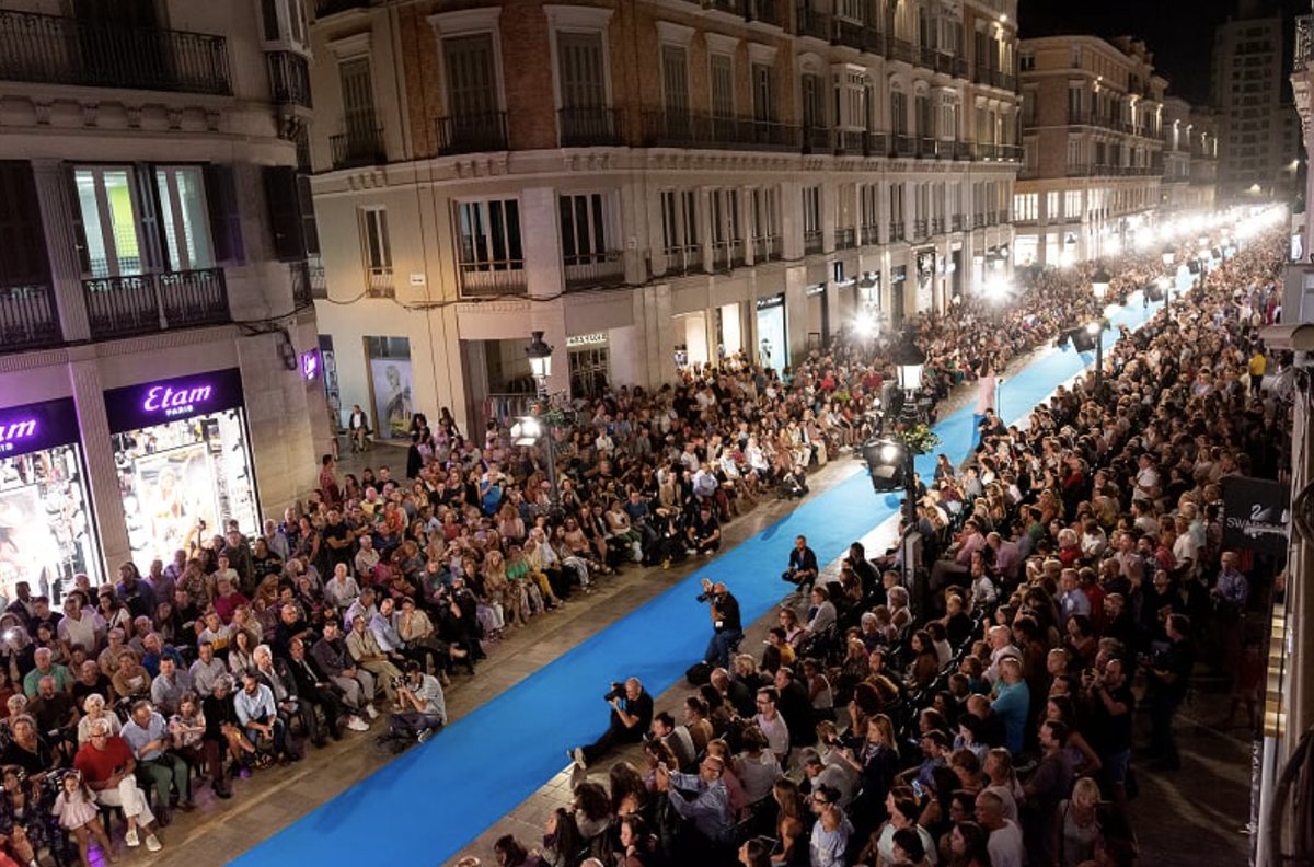 Crowds lining a 350-metre blue carpet catwalk down Calle Larios at night during Málaga Fashion Week